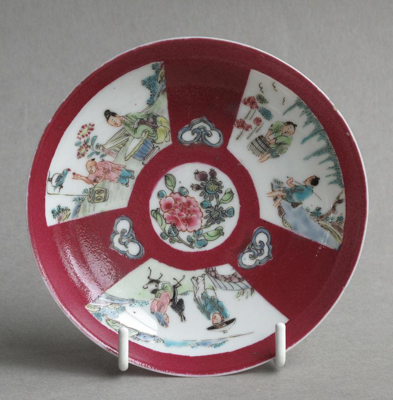A Chinese ruby ground saucer with famille rose panels, dating from the Yongzheng period